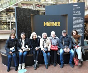 Gruppe sitzt vor einem Schild darauf steht in goldener Schrift "Höhner"